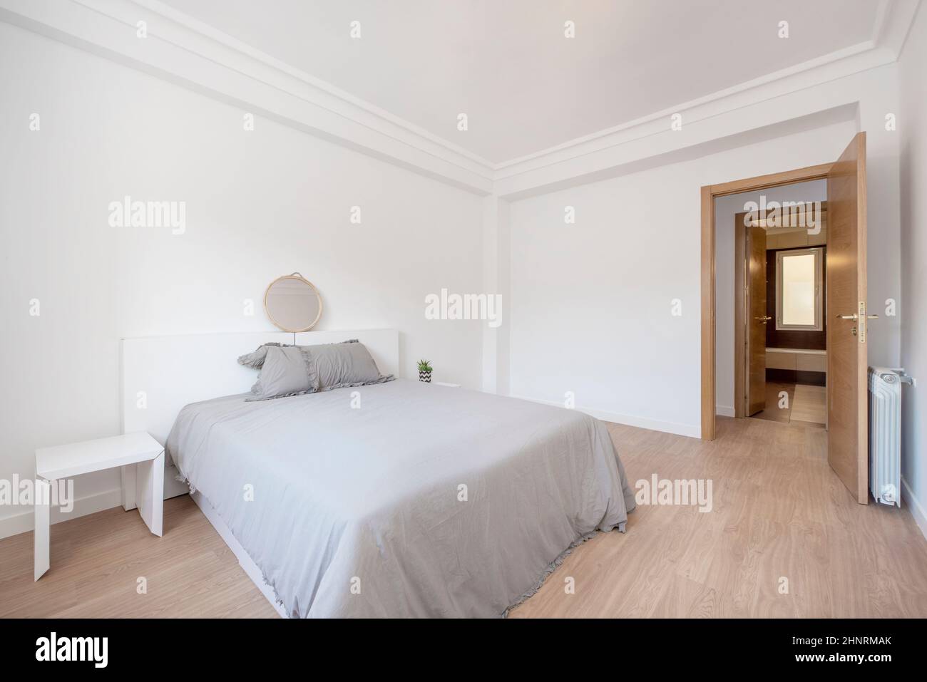 Camera da letto con letto grigio e copriletto con mobili bianchi, radiatore in alluminio e carpenteria in rovere Foto Stock