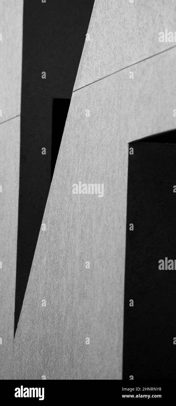 disegno astratto di ombre sulla parete esterna grigia bianca dell'edificio che crea forme geometriche in bianco e nero angoli e linee sfondo verticale Foto Stock