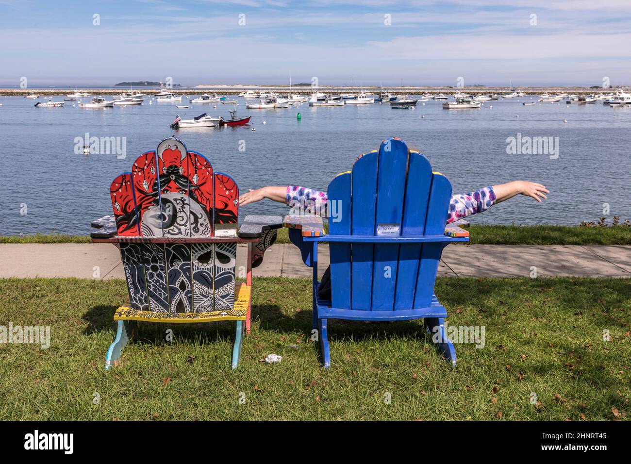 Sedie colorate dipinte da artisti locali sul lungomare di Plymouth con il porto e le navi in background Foto Stock