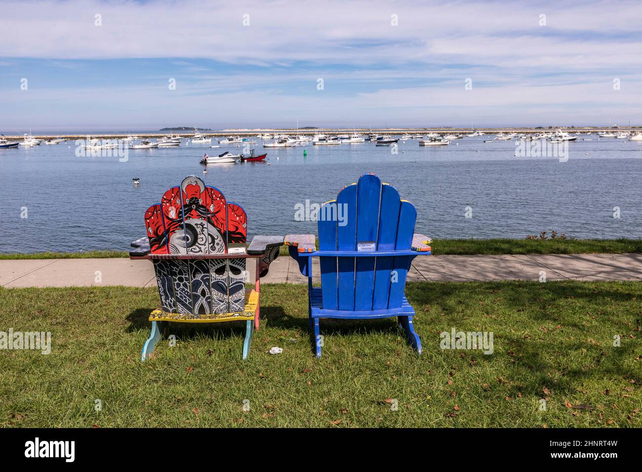 Sedie colorate dipinte da artisti locali sul lungomare di Plymouth con il porto e le navi in background Foto Stock