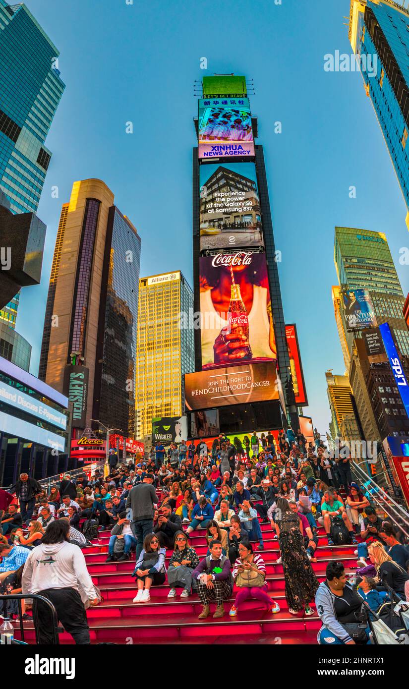 La gente si siede alle scale rosse con la pubblicità al neon delle notizie, dei marchi e dei teatri a Times Square nel tardo pomeriggio Foto Stock