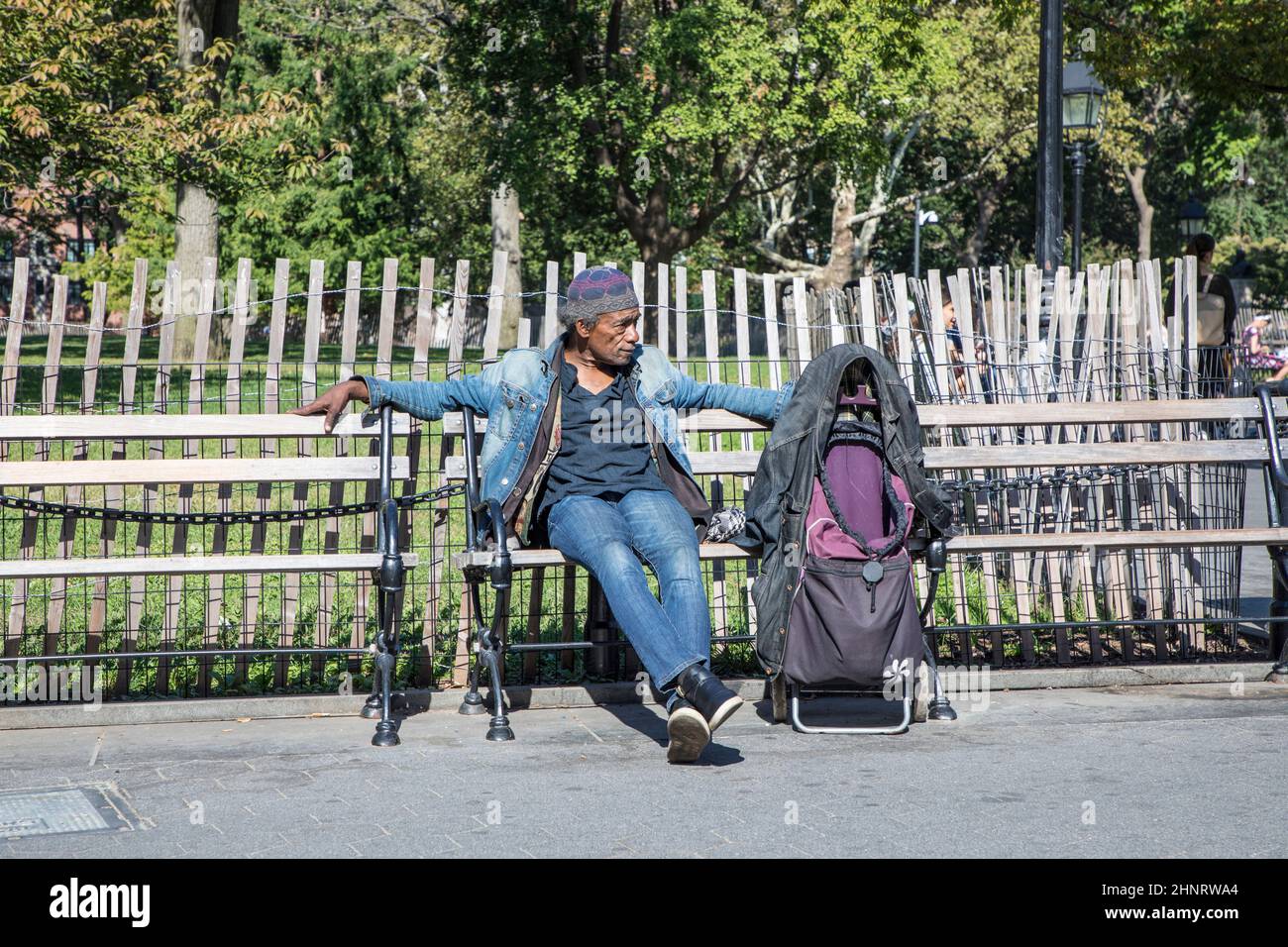 il povero senza tetto siede a una panchina con il suo zaino e i suoi vestiti Foto Stock