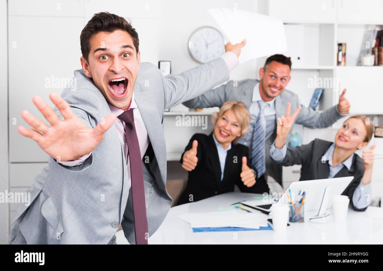 Un uomo d'affari entusiasta con un team felice che celebra la vittoria Foto Stock