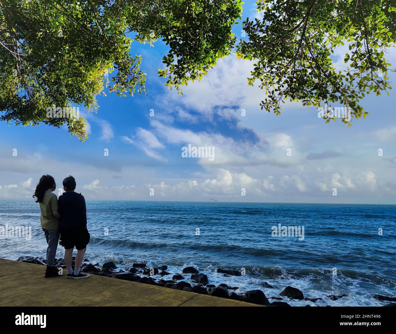 coppia di giovani, un uomo in giacca grigia e una donna in giacca blu denim si affacciano sul mare in una giornata ventosa sullo sfondo Foto Stock