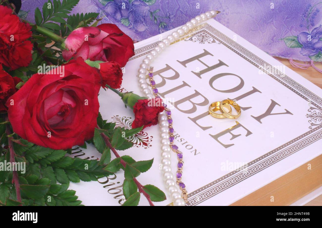 Rose con Bibbia e anelli di nozze su tavola di legno Foto Stock