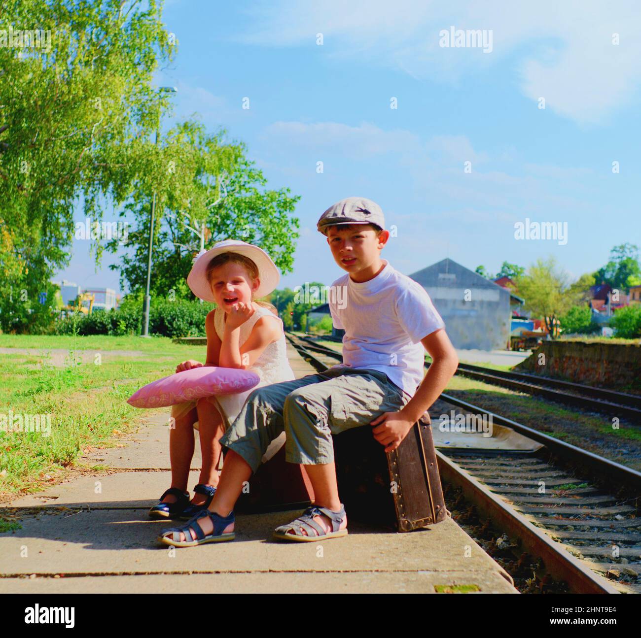 Adorabile bambina e ragazzo su una stazione ferroviaria, in attesa del treno con valige d'epoca. Concetto di viaggio, vacanza e relax. Assicurazione di viaggio concetto Foto Stock
