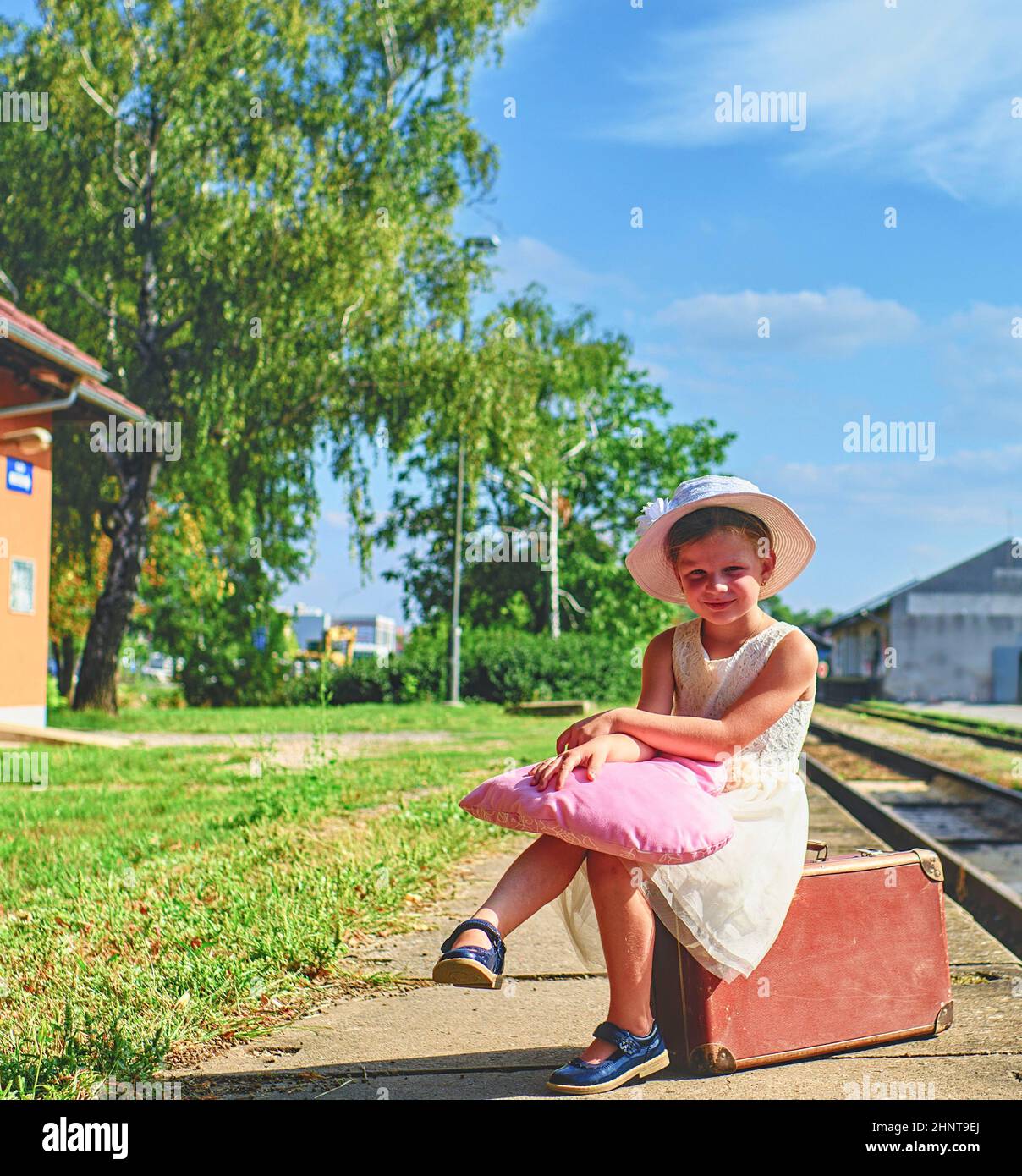 Adorabile bambina su una stazione ferroviaria, in attesa del treno con valigia d'epoca. Concetto di viaggio, vacanza e relax. Assicurazione di viaggio concetto Foto Stock