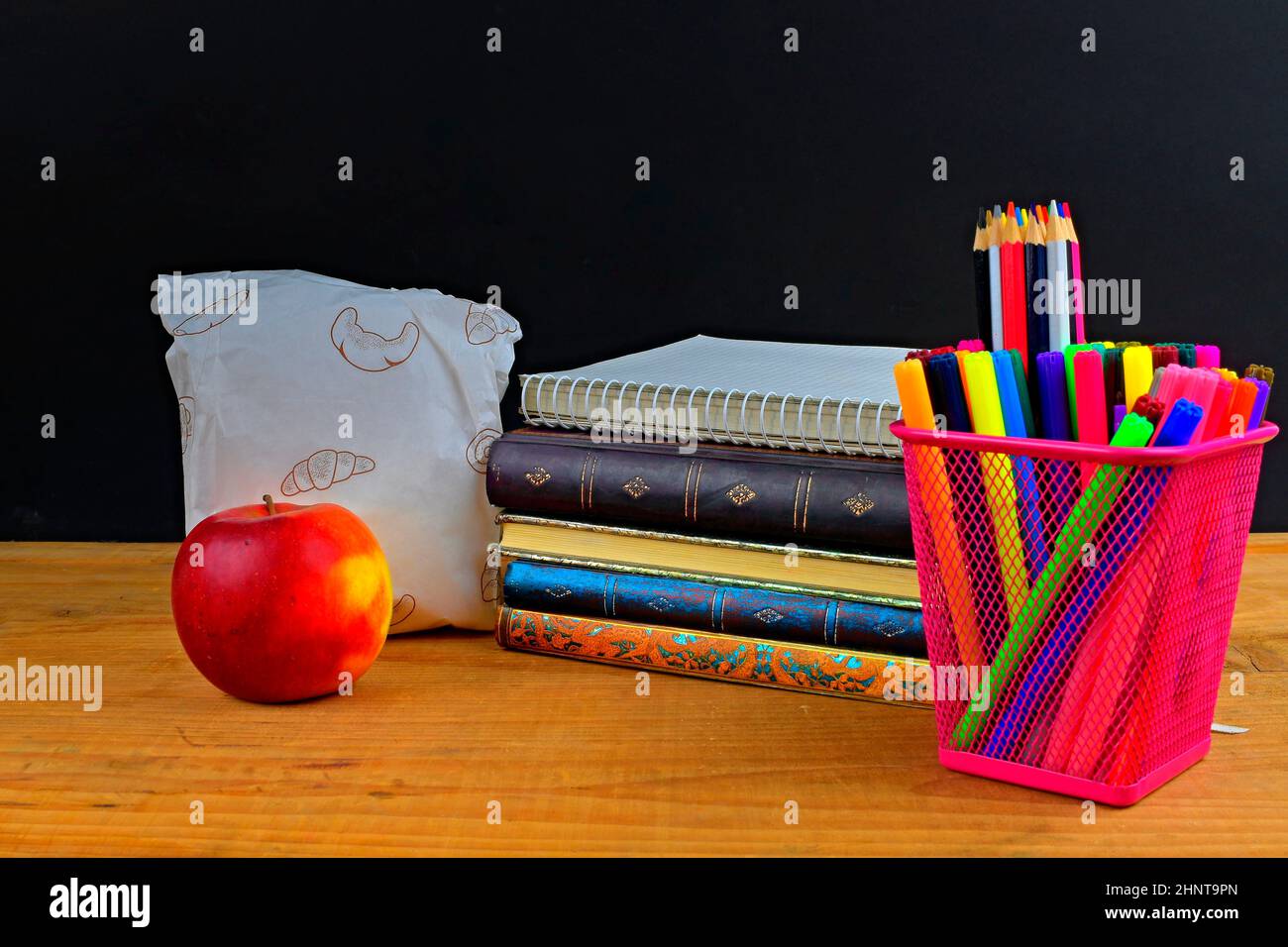 Concetto di pausa pranzo scuola con mela e forniture scolastiche su scrivania in legno, fuoco selettivo. Libri, pennarelli e matite a colori che enfatizzano il concetto. Tempo di studio e relax. Foto Stock