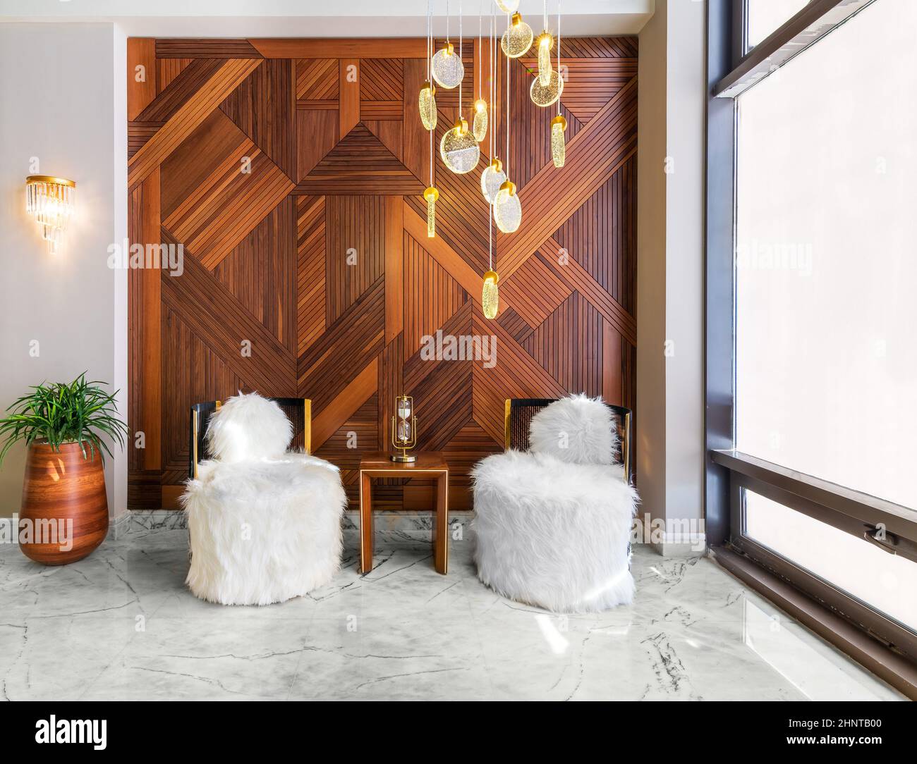 Due moderne sedie senza braccioli in piuma bianca, un tavolino moderno in legno, una pentola e una parete decorata in legno rivestito Foto Stock