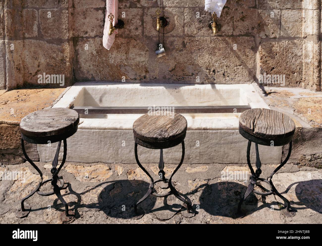 Vista frontale primo piano di rubinetti d'acqua in bronzo islamico d'epoca per la purificazione del corpo e sedie vuote accanto ad una moschea musulmana con backgrou di pietra Foto Stock