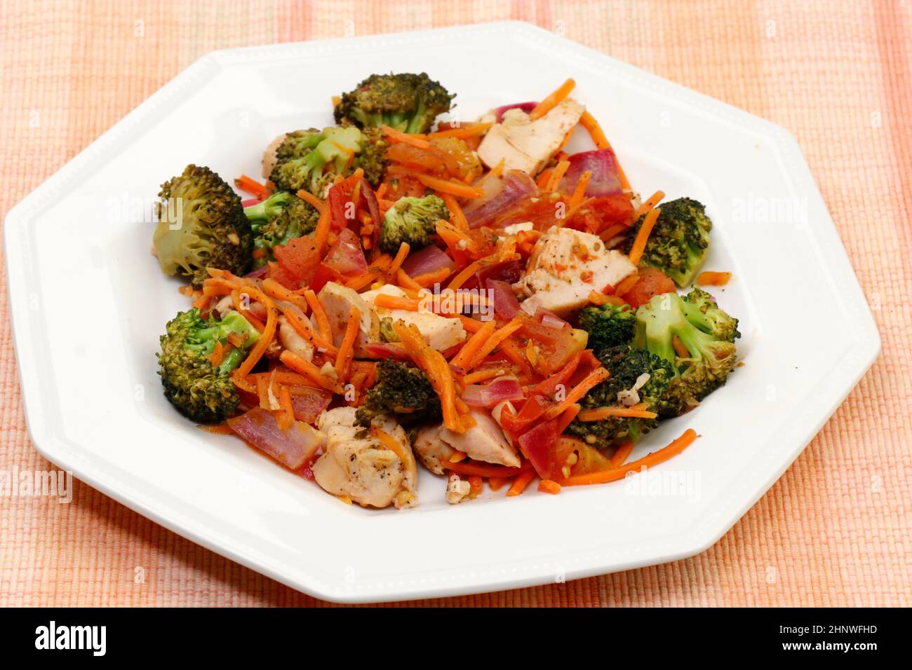 Pasto preparato di carne di pollo con broccoli, carote, cipolla viola e closeup origano. Delizioso pranzo di morsi di pollo con verdure e condimento Foto Stock