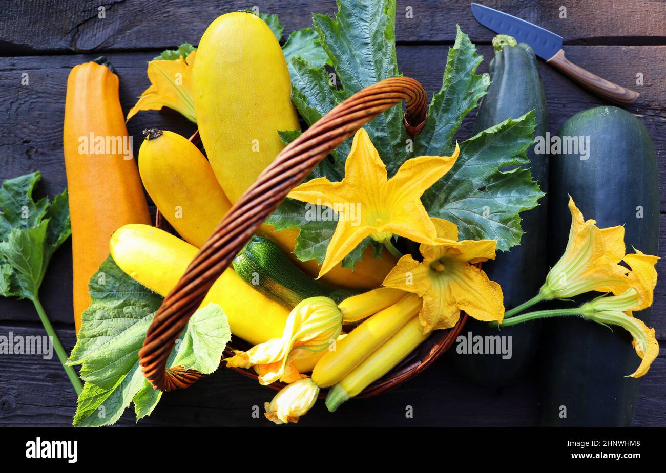 Zucchine fresche in un cestino. Zucchine con fiori sul vecchio rustico tavolo in legno. Foto Stock
