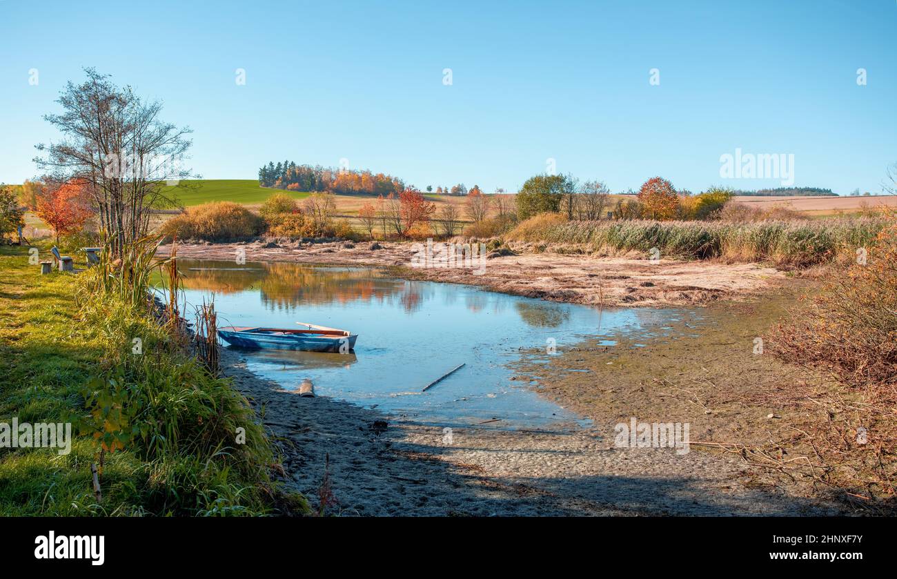 Mattinata d'autunno al laghetto sgocciolato con barca blu, paesaggio di campagna soleggiato, Jihlava Vysocina, Repubblica Ceca Europa Foto Stock