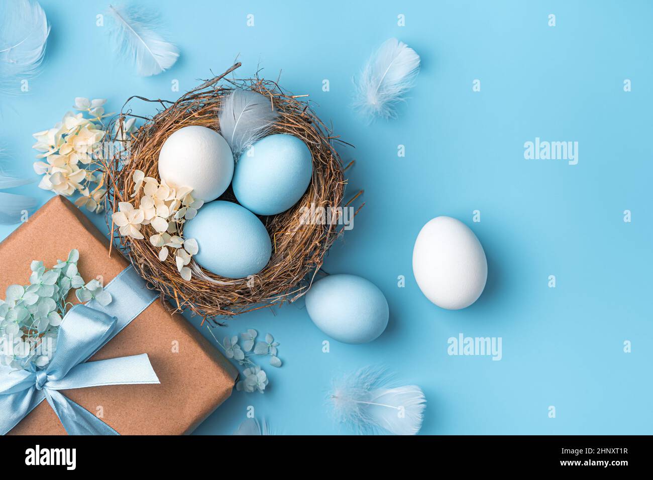 Pasquale pastello sfondo con uova, un nido e un regalo su uno sfondo blu. Il concetto di Buona Pasqua. Vista dall'alto, spazio di copia. Foto Stock