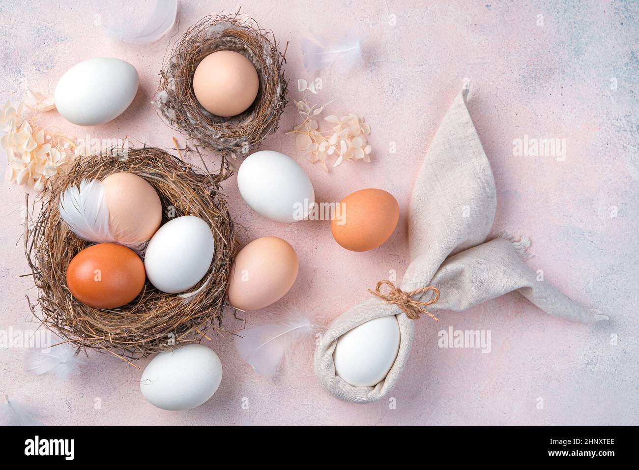 Buona Pasqua, sfondo festivo con uova naturali nel nido e un coniglietto pasquale da un tovagliolo su sfondo rosa chiaro. Vista dall'alto, spazio di copia. Foto Stock