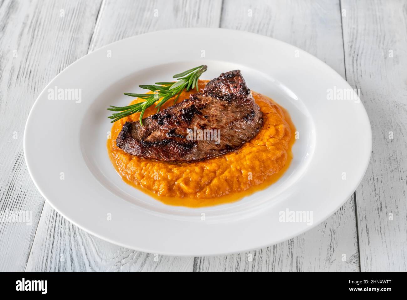 Bistecca di manzo con zucca schiacciata su piatto bianco Foto Stock