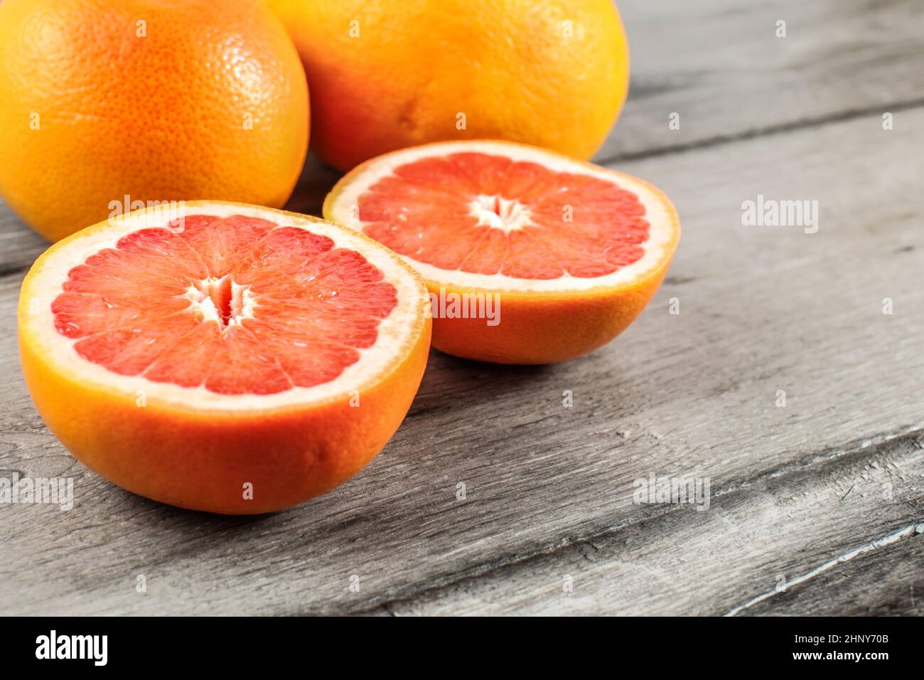 Rosa rosso pompelmo tagliato a metà con due interi in sfondo grigio sulla tavola di legno. Foto Stock
