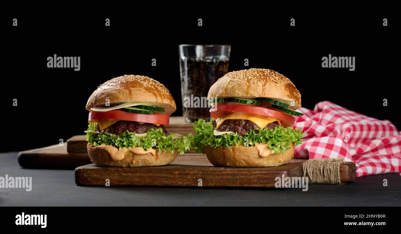 cheeseburger con polpettine di manzo alla griglia, formaggio cheddar, pomodoro e lattuga su un asse di legno, sfondo nero Foto Stock