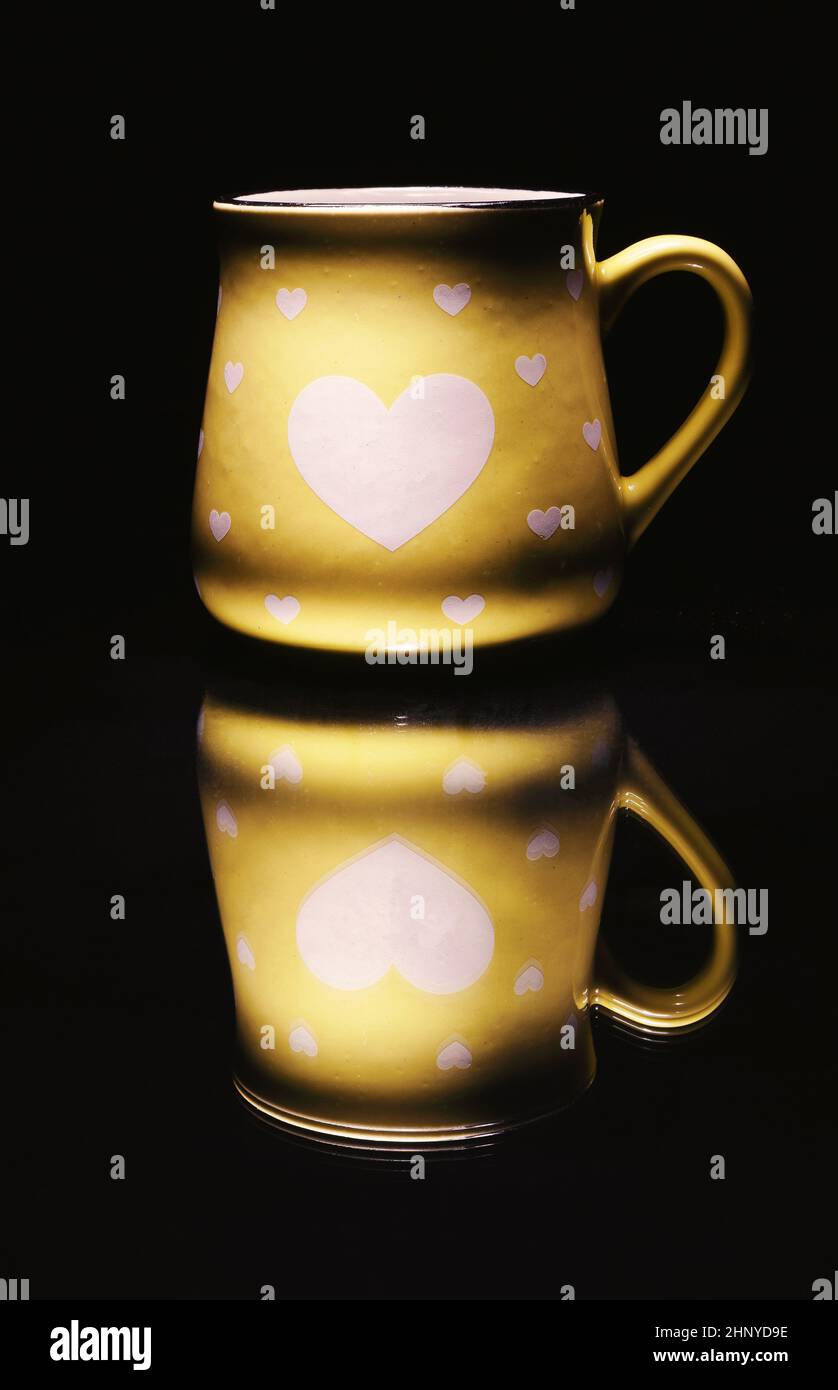 Una tazza gialla con i cuori sullo specchio, sfondo nero. Foto Stock