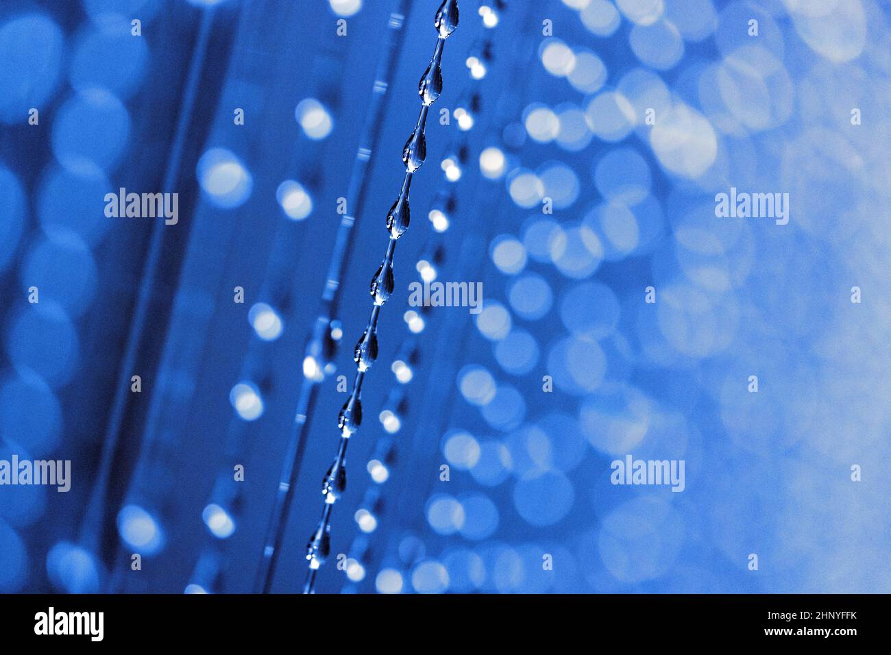 Primo piano di una grande quantità di gocce d'acqua che scorrono lungo i fili con luce blu. Profondità di campo poco profonda. Foto Stock