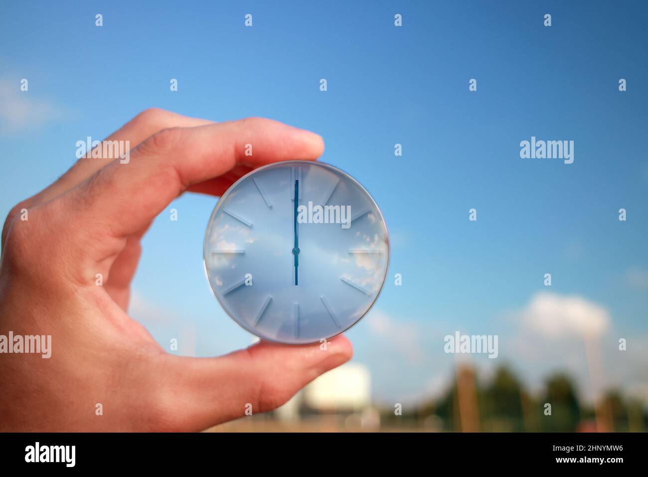 Il quadrante di un orologio in una mano contro uno sfondo di cielo blu. Dodici del pomeriggio sul quadrante dell'orologio. Foto Stock