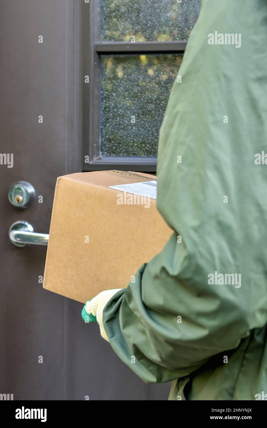 Scatola di cartone nelle mani del postino sullo sfondo della porta della casa. Consegna del servizio di corriere pacchi a casa vostra. Foto Stock