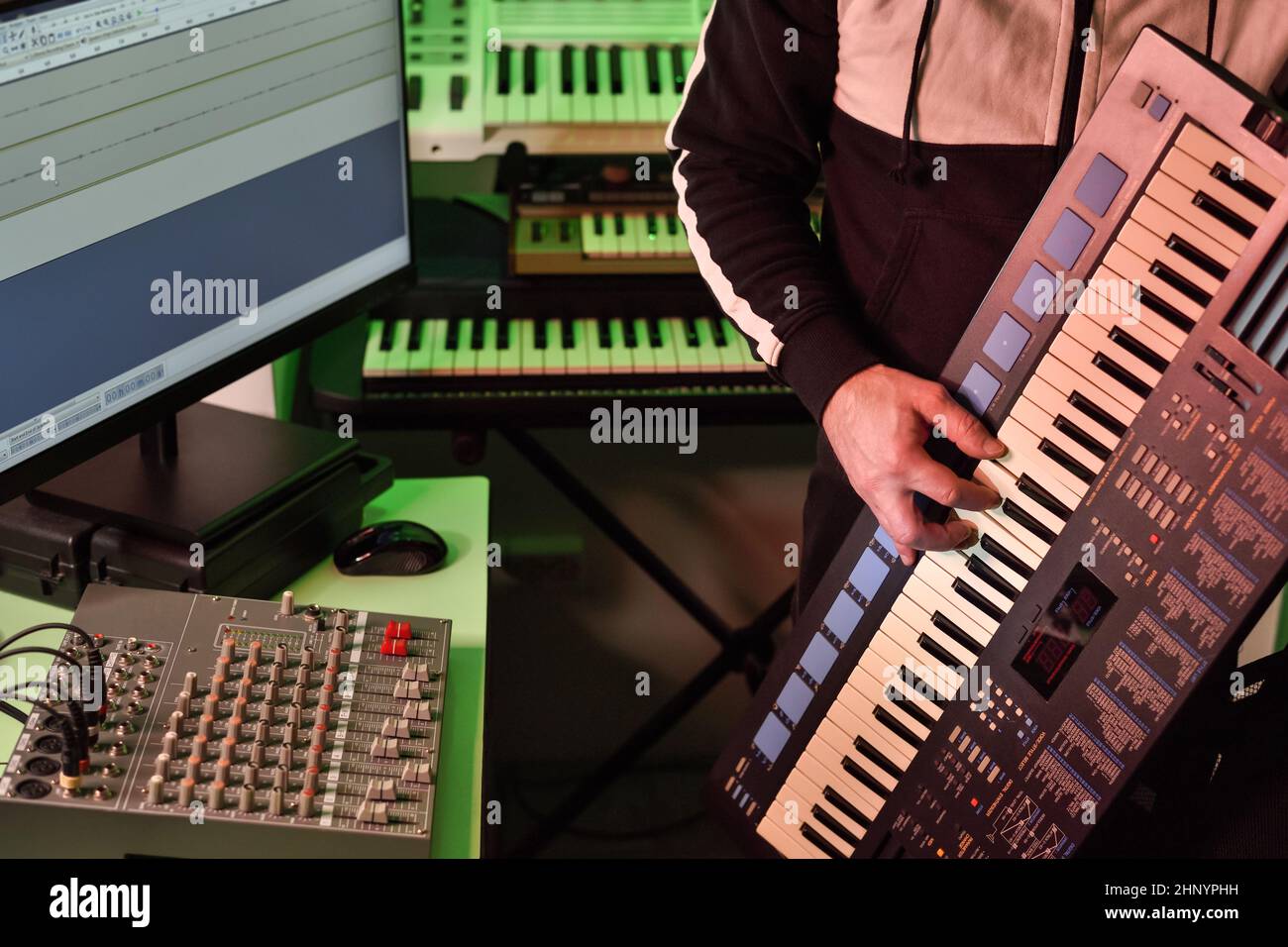 Il musicista suona il sintetizzatore nel piccolo studio mentre crea e registra musica elettronica. Foto Stock