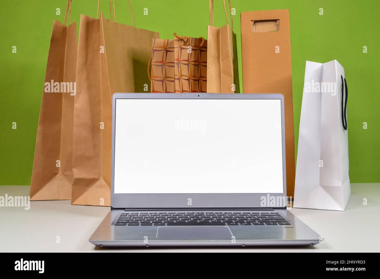 Schermo bianco su un laptop sullo sfondo di sacchetti di carta con merci e acquisti ordinati nel mercato online e consegnati a casa Foto Stock