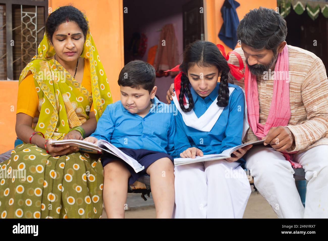 I genitori indiani tradizionali aiutano i loro bambini piccoli negli studi, il ragazzo e la ragazza nella uniforme della scuola che studiano nel paese. Madre che porta sari e padre dentro Foto Stock