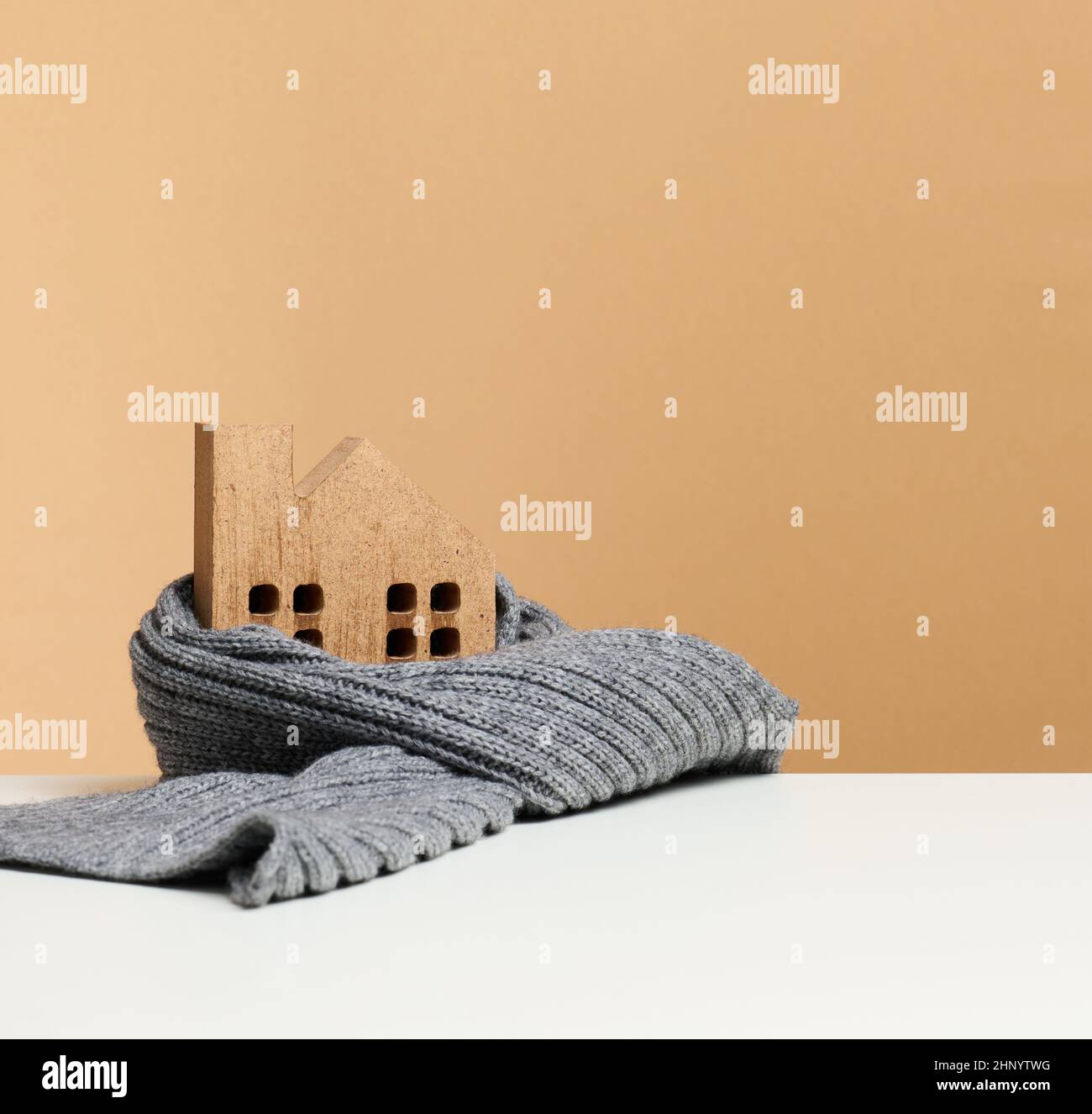 casa in miniatura in legno marrone avvolta in una sciarpa di maglia grigia. Costruzione di isolamento concetto, prestiti per le riparazioni Foto Stock