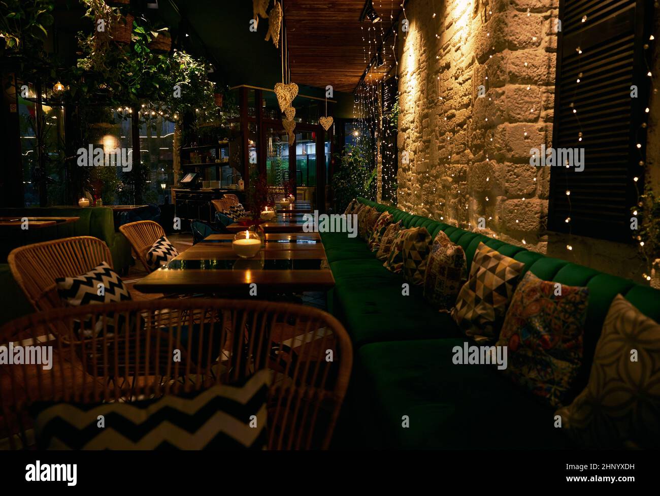 Modello di candele bruciate su tavoli di legno e cuscini sul divano con riflessi retroilluminati sui tavoli. Foto Stock