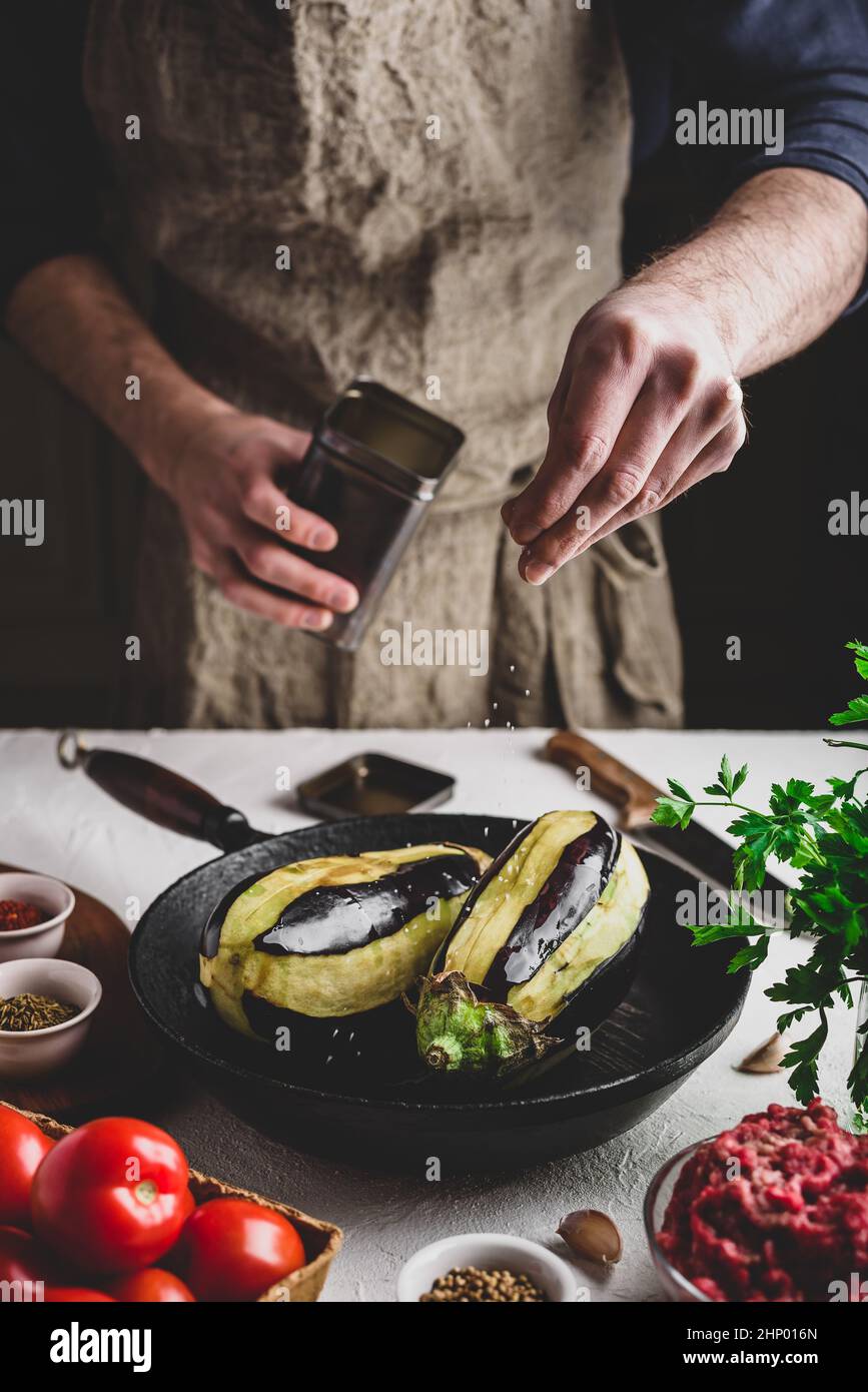 Preparazione delle melanzane per la cottura e ripieno con carne macinata e pomodori. Sale spruzzante Foto Stock
