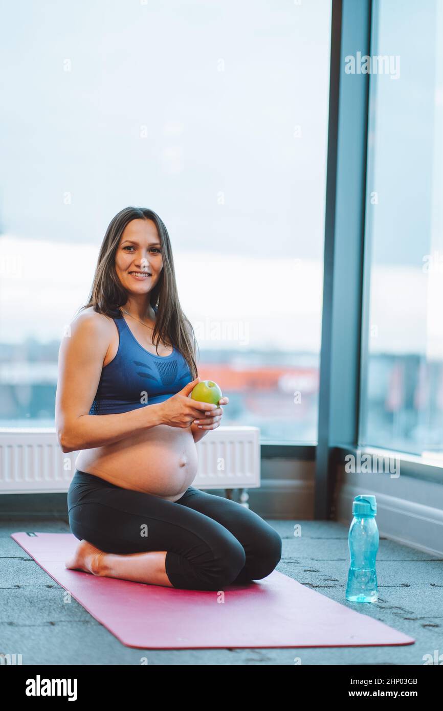 Fitness verticale atletica piuttosto donna incinta, facendo yoga, seduta gambe piegate Foto Stock