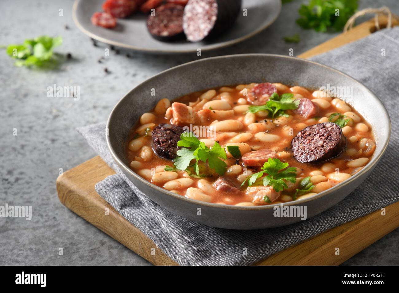 Stufato spagnolo fabada con chorizo, morcilla, salsiccia, haricot servito toast fresco su tavola grigia. Primo piano. Cena tradizionale riscaldata. Foto Stock