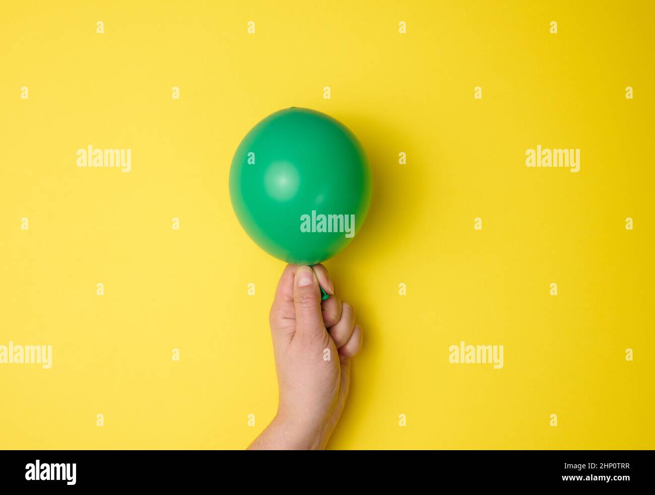 mano femmina che tiene un palloncino di aria verde gonfiato su uno sfondo giallo, primo piano Foto Stock
