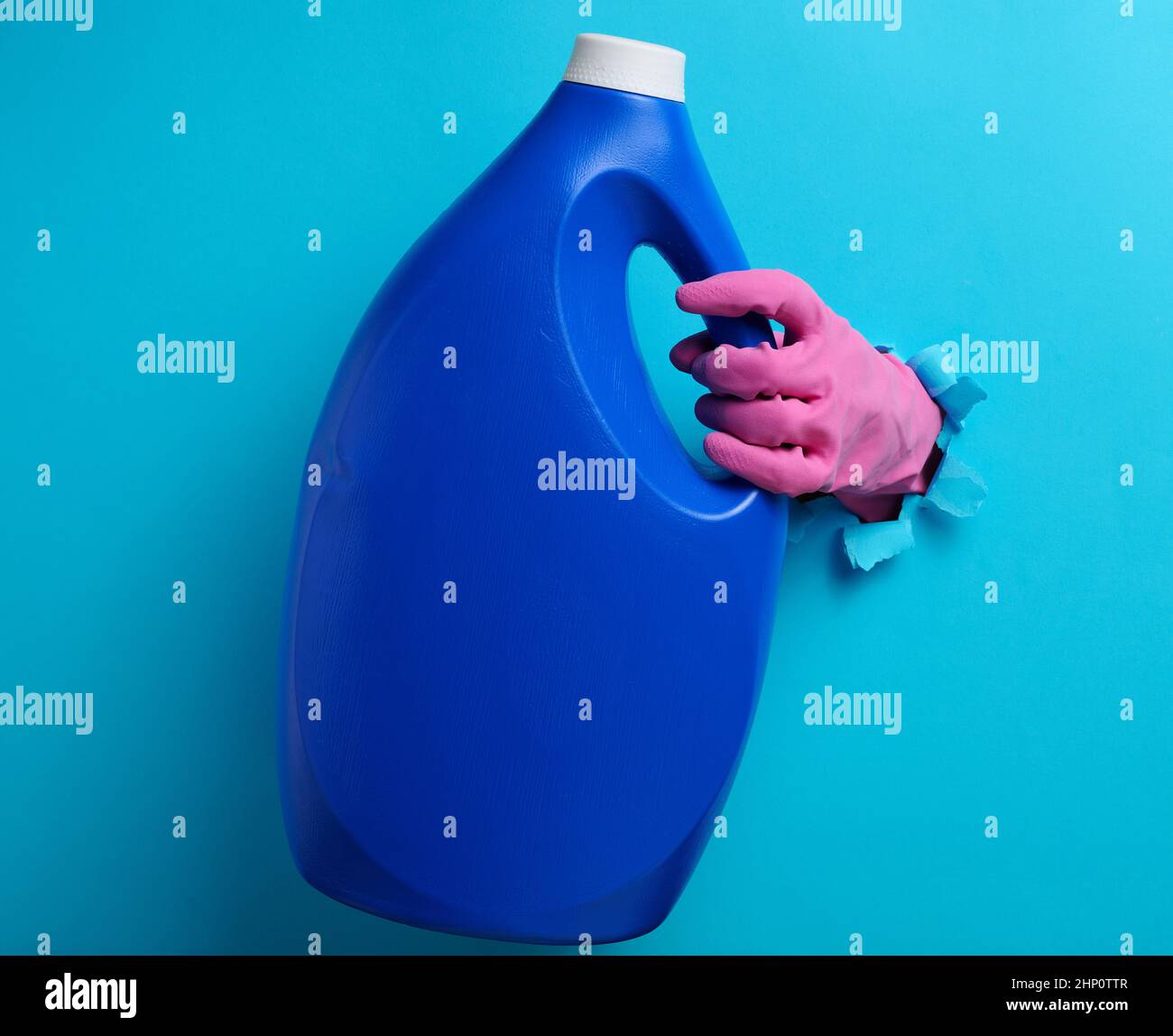 bottiglia di plastica blu con detergente liquido in una mano femmina su sfondo blu. Una parte del corpo sporge da un foro lacerato sullo sfondo Foto Stock