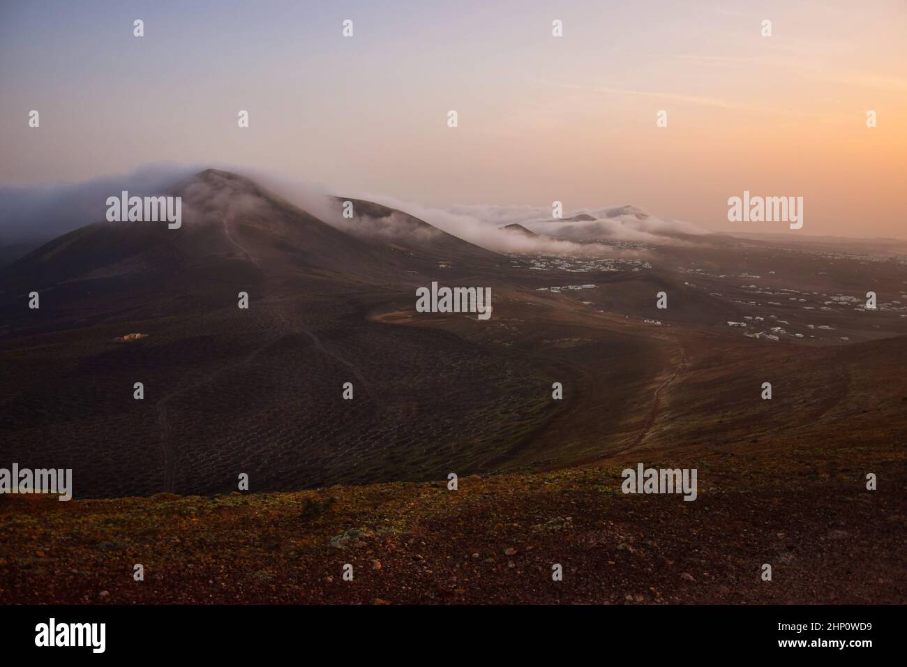 Alba a Lanzarote. Le nuvole di vento di commercio stanno venendo sopra le montagne e si dissolve. Isole Canarie, Spagna. Foto Stock