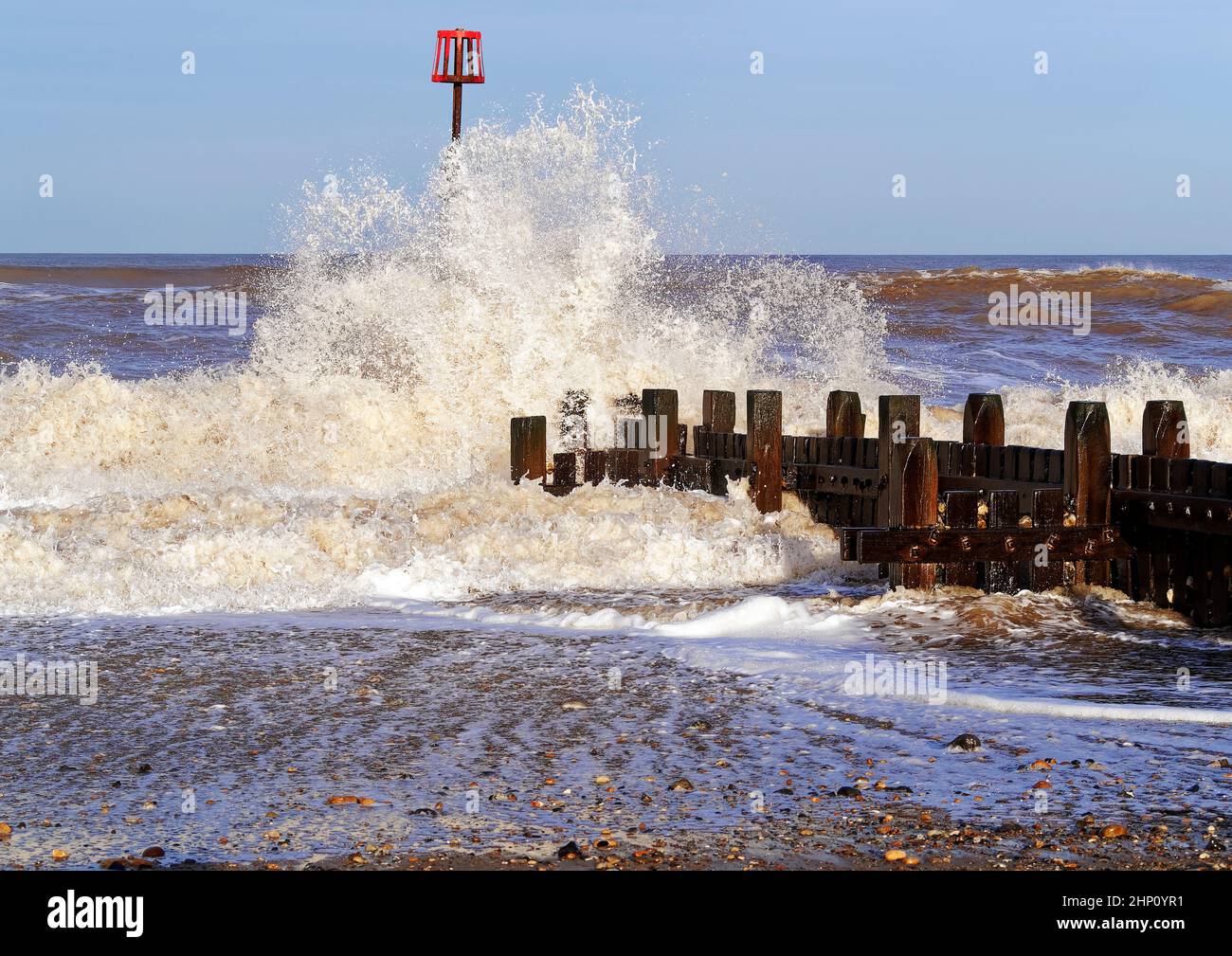 Onde che si infrangono sulle difese del mare di legno a Walcott, Norfolk durante i mari accidentati a seguito di una tempesta che provoca spruzzi e schiuma di mare. Foto Stock