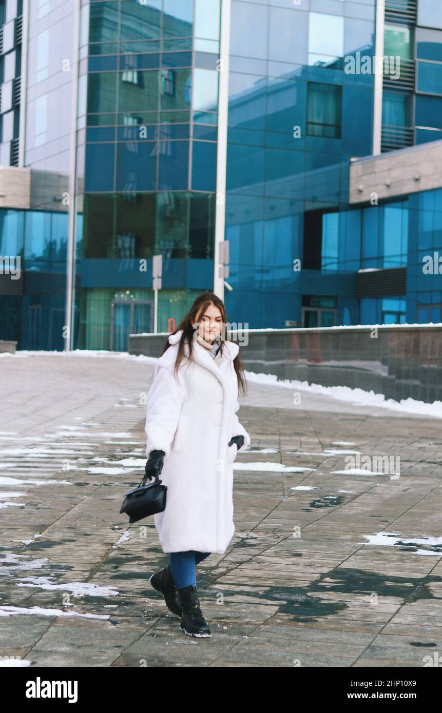 Ritratto urbano di giovane donna elegante in inverno abiti casual, giacca bianca. Camminando nella strada della città, parlando al telefono, facendo selfie Foto Stock