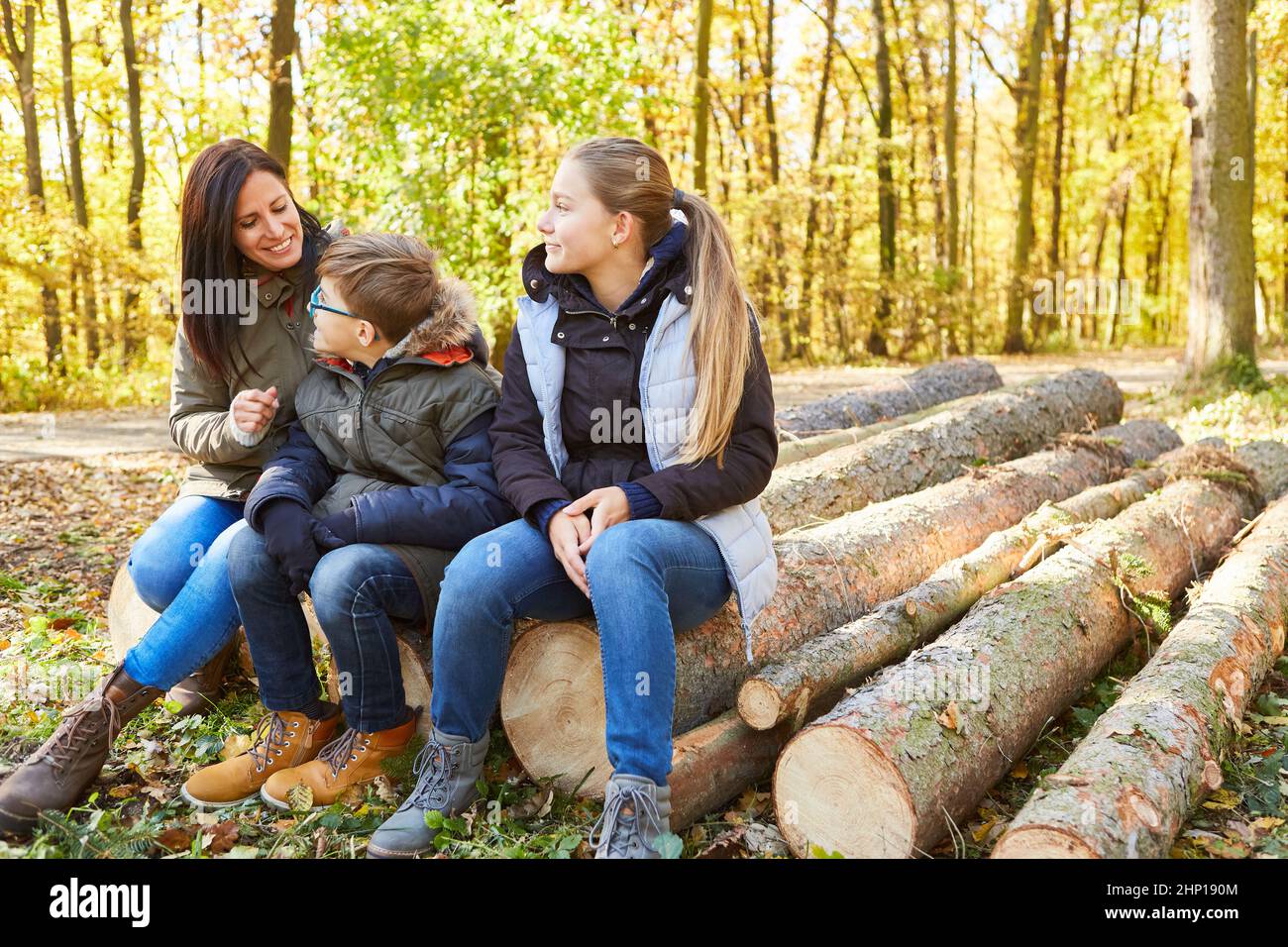 Due bambini e una madre si siedono rilassati sui tronchi d'albero durante un'escursione nella natura nella foresta Foto Stock