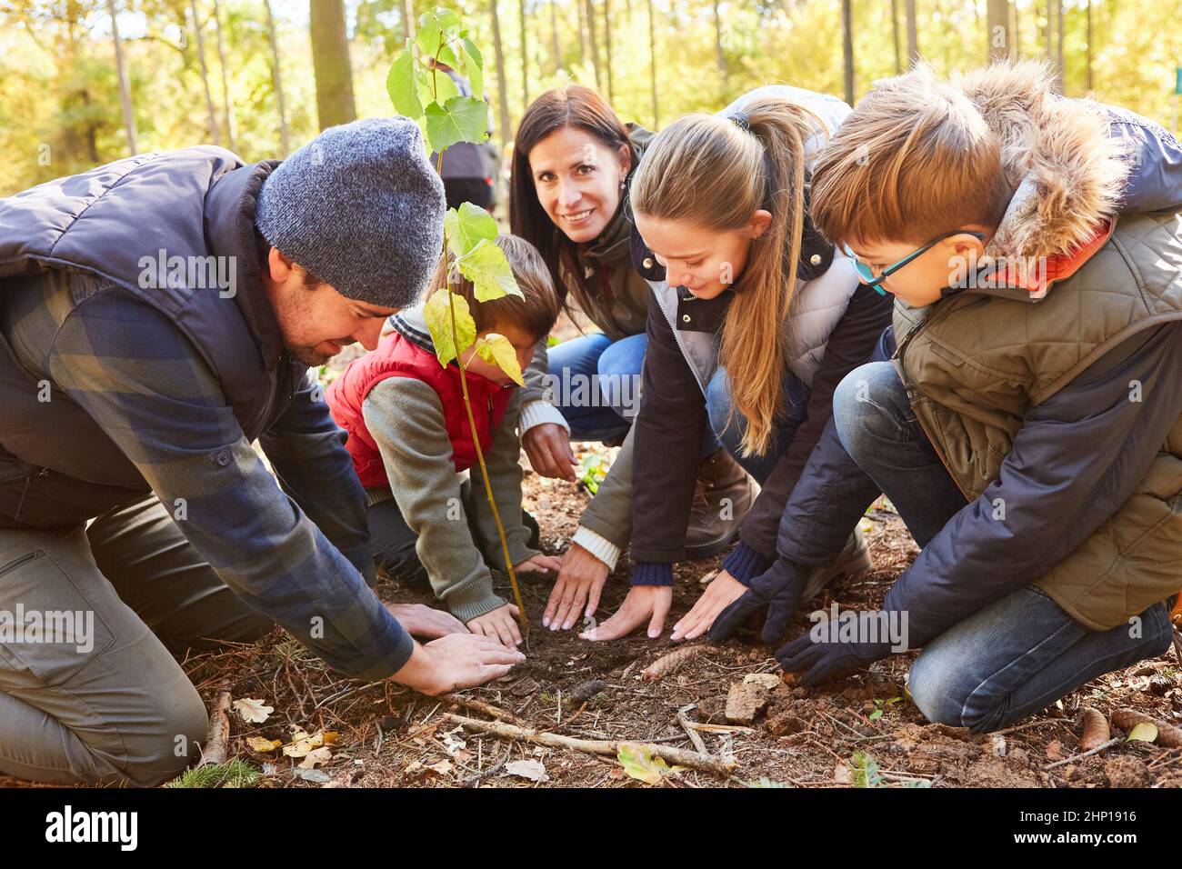 Forester e famiglia con bambini piantando alberi insieme nella foresta Foto Stock