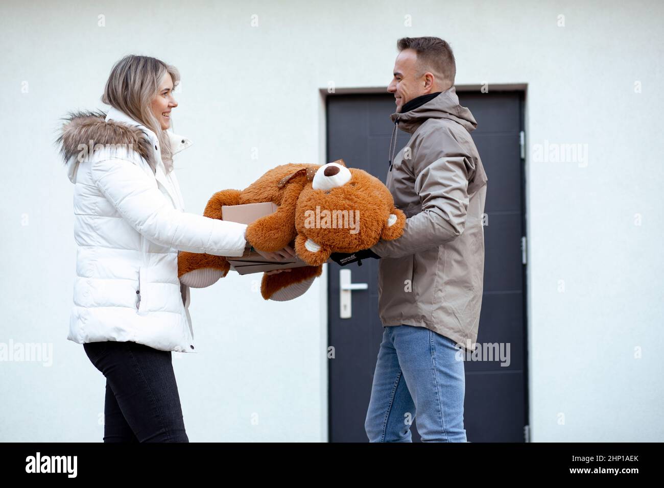 Ritratto di felice sorridente coppia carina in abiti casual superiore stand tenendo enorme orsacchiotto arancione e scatola di cartone. Foto Stock