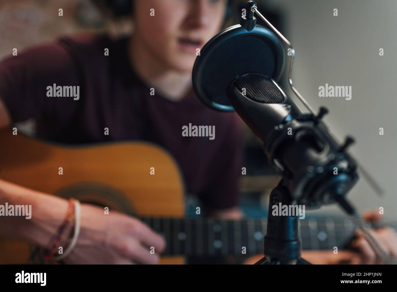 Microfono con filtro pop closeup foto con un ragazzo giovane in cuffie registrazione voce e chitarra suonare musica. Moderno studio di home sound au Foto Stock