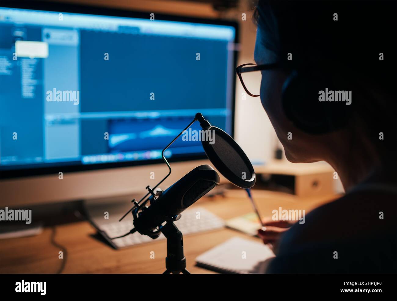 Microfono con filtro pop closeup foto con una giovane donna in cuffie registrazione voce utilizzando un computer desktop con applicazione Music Creation Studio. Mod Foto Stock
