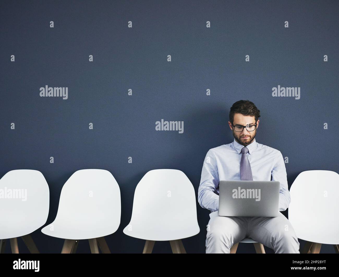 Venne preparato. Studio girato di un giovane uomo d'affari usando un laptop mentre aspettava in fila su uno sfondo grigio. Foto Stock