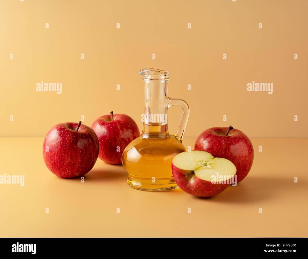 Aceto di mele in un contenitore di vetro su sfondo beige con un sacco di mele intorno. Foto Stock