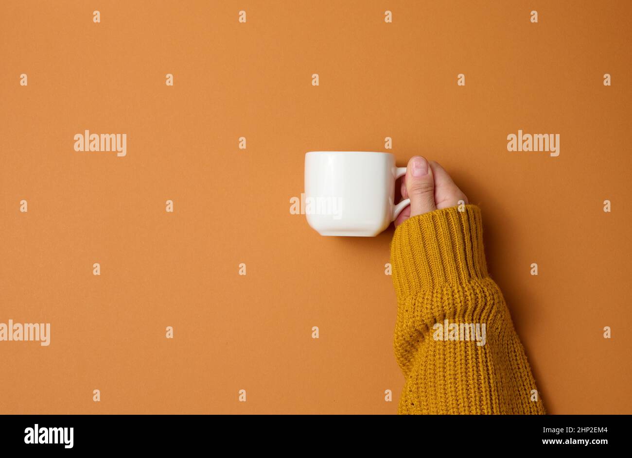 tazza in ceramica bianca in una mano femmina su sfondo arancione, bevanda e mano sono alzate, pausa caffè Foto Stock