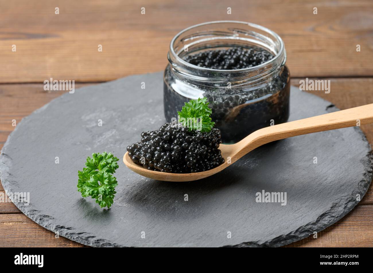 caviale di paddlefish nero sgranato fresco in cucchiaio di legno marrone su un tavolo marrone, primo piano Foto Stock
