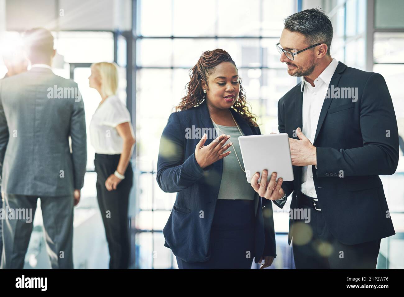 Pianificazione digitale in azione. Foto di due colleghi che parlano insieme su un tablet digitale in ufficio. Foto Stock