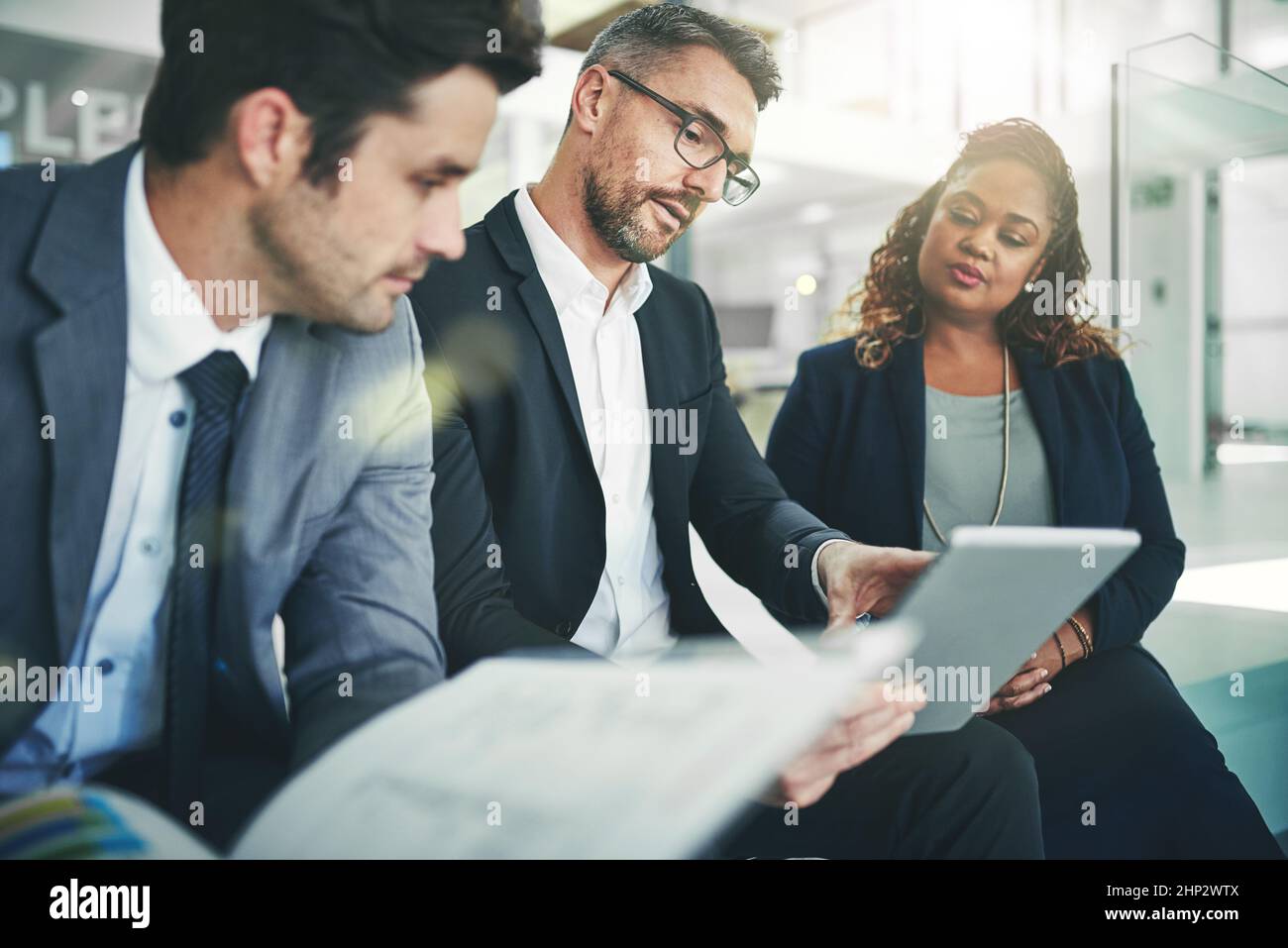 Condividere il suo acume aziendale. Foto di un gruppo di colleghi che parlano insieme su un tablet digitale in ufficio. Foto Stock